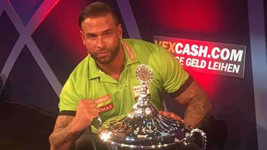 Tim Wiese kniet neben dem Promi-Darts WM-Pokal im Januar 2017